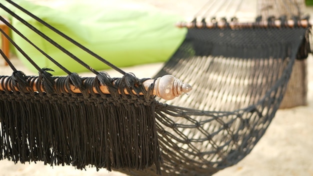 Hamac Noir Qui S'étend Entre Les Cocotiers. Hamac En Filet Avec Frange Sur La Plage De Sable Paradisiaque.