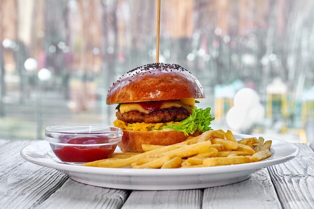 Hamburger avec escalope de boeuf fromage frites sauce salade de tomates et ketchup sur une assiette