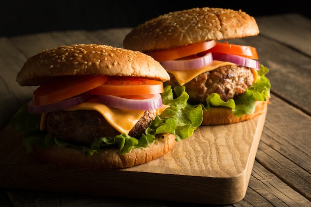 Hamburger fait maison avec boeuf, oignon, tomate, laitue et fromage. Burger frais bouchent sur table rustique en bois avec frites de pommes de terre, bière et frites. Cheeseburger.