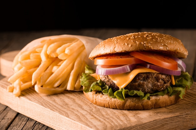 Hamburger fait maison avec boeuf, oignon, tomate, laitue et fromage. Burger frais bouchent sur table rustique en bois avec frites de pommes de terre, bière et frites. Cheeseburger.