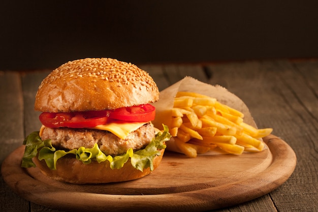 Hamburger fait maison avec boeuf, oignon, tomate, laitue et fromage. Burger frais bouchent sur table rustique en bois avec frites de pommes de terre, bière et frites. Cheeseburger.