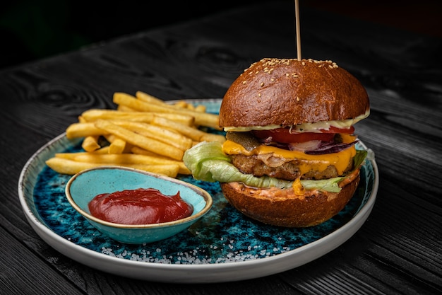 Hamburger avec frites et sauce sur une table en bois foncé