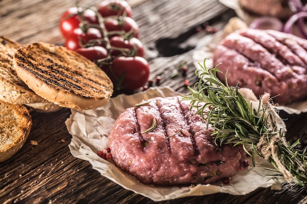 Hamburgers crus sur table en bois avec oignons tomates herbes et épices.