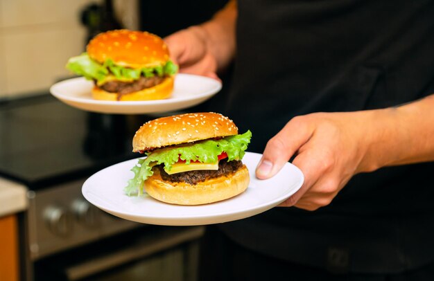 Des hamburgers faits maison avec du fromage, des tomates, des feuilles de salade verte sur une grande assiette.