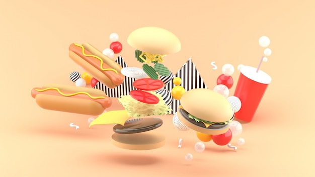 Hamburgers, hot-dogs et boissons gazeuses parmi des boules colorées sur orange. Rendu 3D.