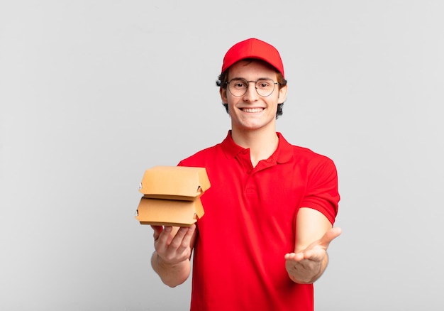 Les hamburgers livrent un garçon souriant joyeusement avec un regard amical, confiant et positif, offrant et montrant un objet ou un concept