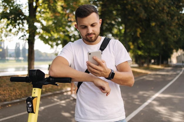 Hamdsome man using phone pendant la pause befour riding on escooter