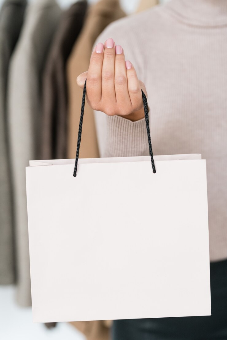 Photo hand of female shopaholic holding white paperbag avec achat en se tenant debout dans la boutique lors de la vente