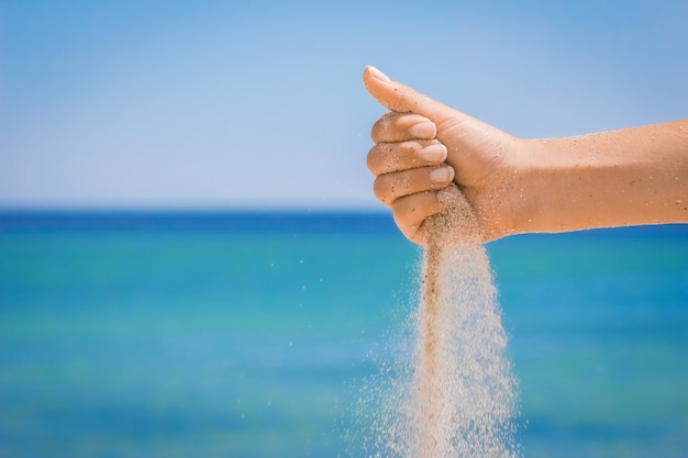 A Hands déversent le sable de la mer sur la nature lors d'un voyage. Les vacances en mer, le temps passe.