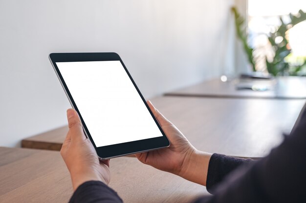 Hands holding black tablet pc avec écran blanc vide alors qu'il était assis au bureau