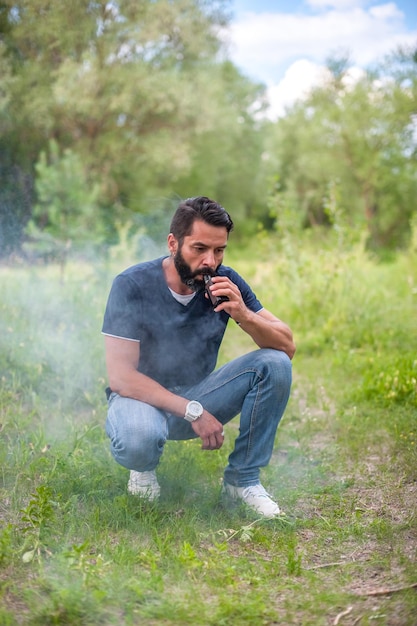 Handsomesmoker fume vape exhale de la fumée dans la forêt. Activité de vapotage.