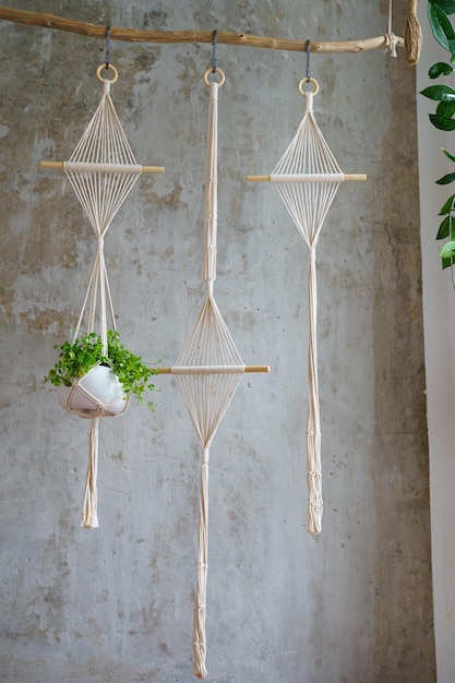 Photo hanger de plante de macrame de coton fait à la main suspendu à une branche de bois sur un mur gris à la maison