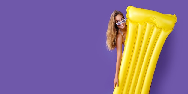 Happy adult girl in bikini va voter avec fond de studio violet matelas gonflable jaune