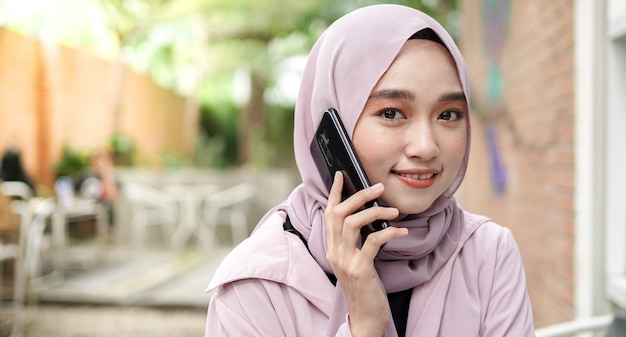 Happy Asia hijab woman using smart phone et appelant, boire du café assis au café