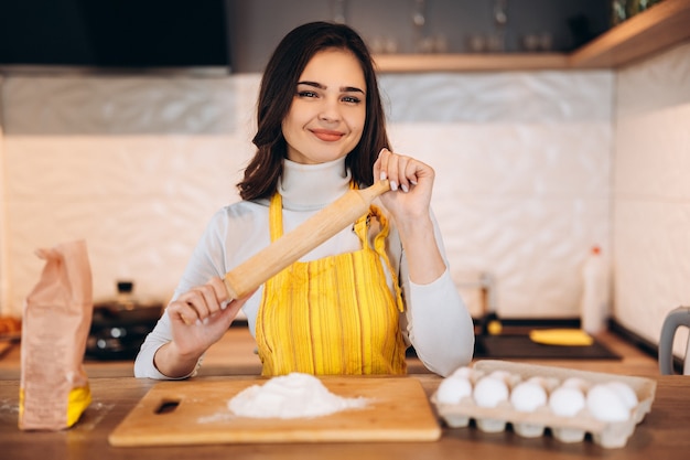 Happy attractive young adult woman lady femme au foyer boulanger porter tablier sur table de cuisine cuisson pâtisserie concept cuisson gâteau biscuit faire boulangerie faire pizza maison à la maison.