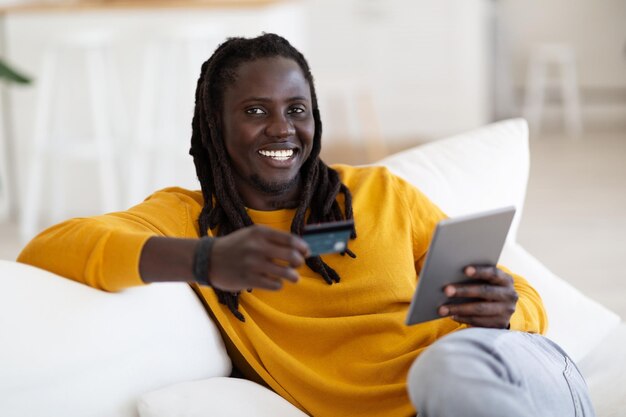 Happy Black Guy utilisant une tablette numérique et une carte de crédit pour les paiements en ligne