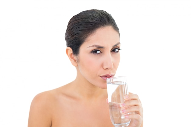 Happy brunette en sirotant un verre d&#39;eau et en regardant la caméra