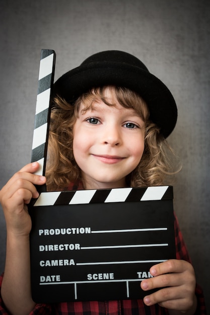 Happy child holding clapper board sur fond de mur de grunge. Concept de cinéma