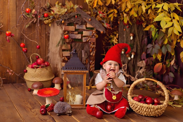 Photo happy fairytale little gnome baby girl jouer et ramasser des citrouilles, des champignons, manger des pommes