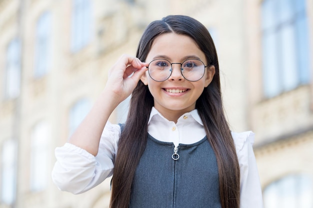 Happy Girl Enfant Portant L'uniforme Scolaire Fixer Des Lunettes Dans Le Cadre De La Mode Pour Voir Clairement Les Opticiens à L'extérieur