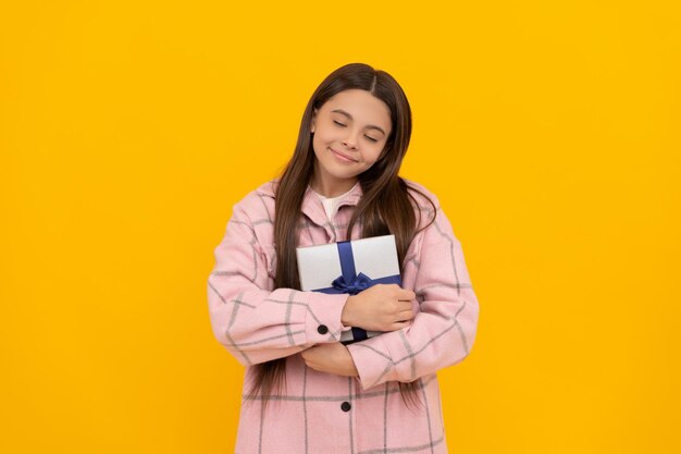 Happy girl enfant sourire avec les yeux fermés holding gift box fond jaune, présent