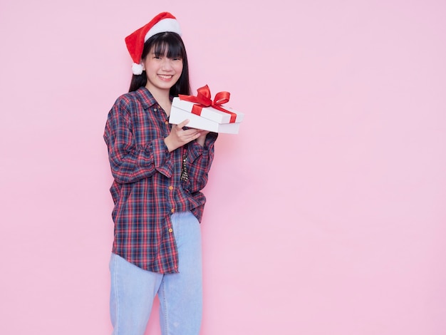 Happy girl in Santa hat ouvrant une boîte-cadeau contre le mur rose