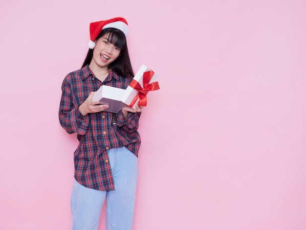 Happy girl in Santa hat ouvrant une boîte-cadeau contre le mur rose