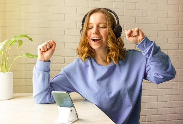 Happy girl utilise des écouteurs pour écouter de la musique ou discuter en ligne.