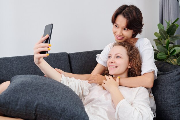 Happy hugging multi-ethnic couple prenant selfie pour les médias sociaux sur smartphone