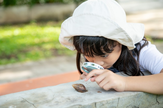 Happy kid girl explorant la nature avec une loupe et un escargot. Il s'amuse dans le jardin. Le concept de l'enfant est prêt à aller à l'école.