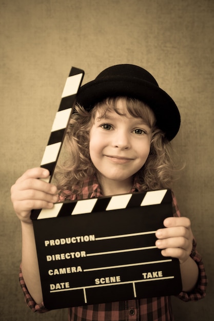 Happy kid holding clapper board sur fond de mur de grunge. Concept de cinéma