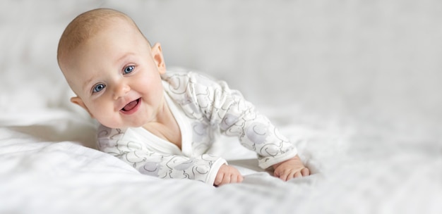 Happy little baby girl smiling allongé sur le lit sur un drap blanc à la maison en regardant la caméra. Copiez l'espace pour le texte, la maquette, la bannière