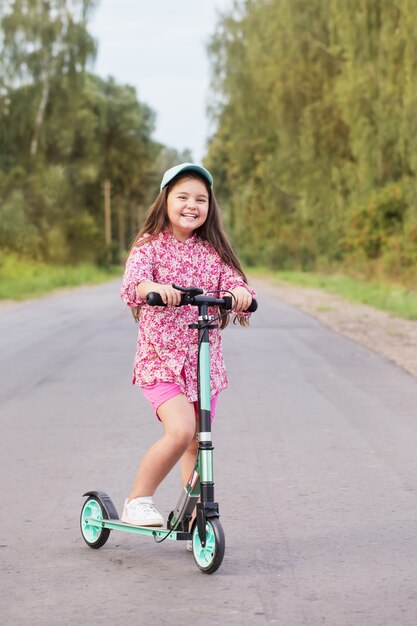 Happy little girl riding scooter sur route de campagne