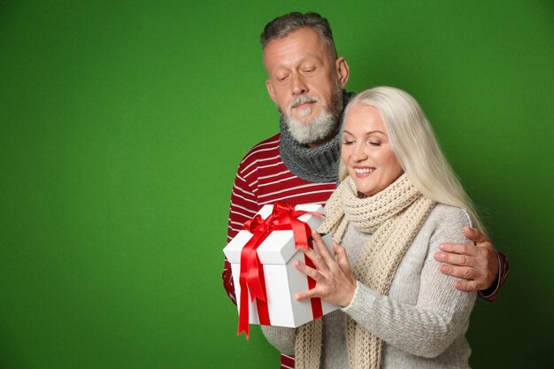 Happy senior couple avec cadeau de Noël sur fond de couleur