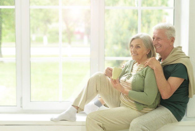 Happy Senior couple drinking tea assis sur le rebord de la fenêtre à la maison