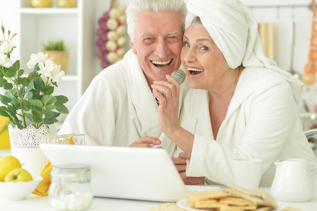 Happy senior couple in a peignoirs avec ordinateur portable à la maison