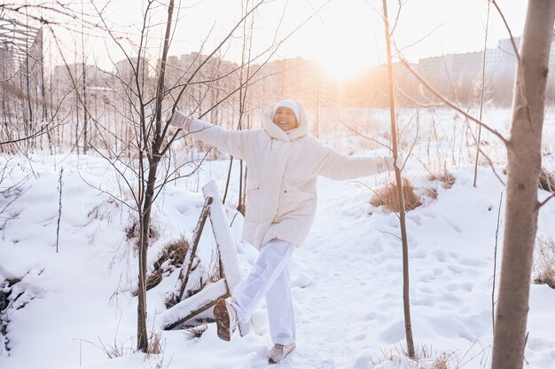 Happy senior senior woman in white outwear chaud jouant avec la neige en plein air d'hiver ensoleillé