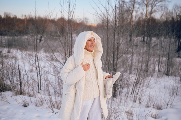 Happy senior senior woman in white outwear chaud jouant avec la neige en plein air d'hiver ensoleillé