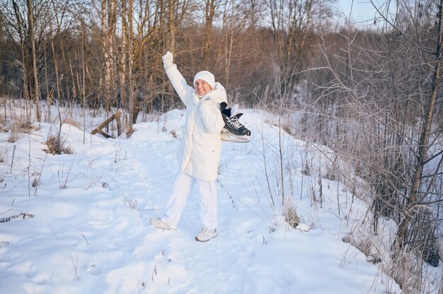 Happy senior senior woman in white outwear chaud jouant avec des patins à glace en hiver neigeux ensoleillé à l'extérieur