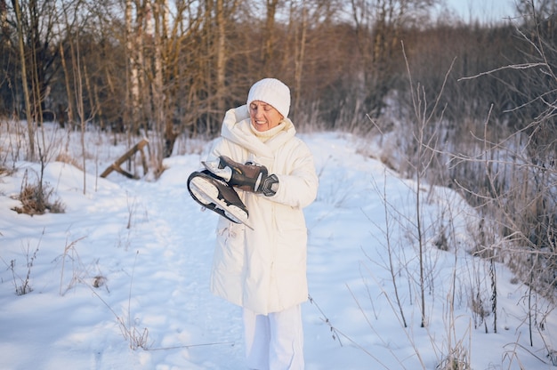 Happy senior senior woman in white outwear chaud jouant avec des patins à glace en hiver neigeux ensoleillé à l'extérieur