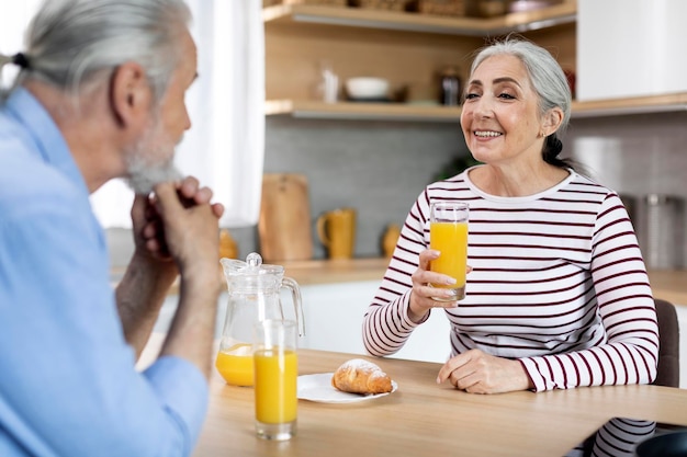 Happy Senior Woman Drinking Juice tout en prenant le petit déjeuner avec son mari dans la cuisine