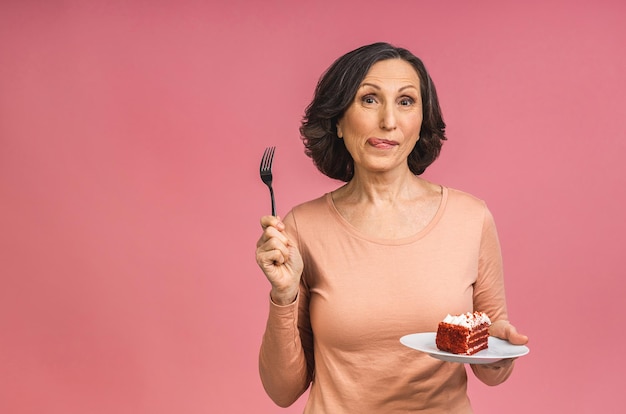 Happy smiling mature senior woman holding a birthday cake isolé sur fond rose.