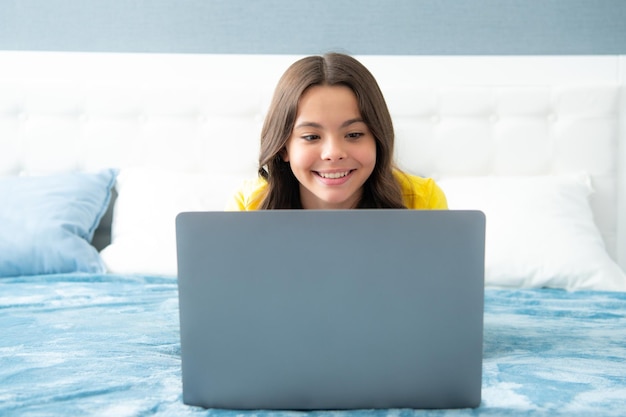 Happy teen adolescente sur le lit à la maison à l'aide d'un ordinateur portable Enfant naviguer sur Internet sur la communication d'amitié informatique