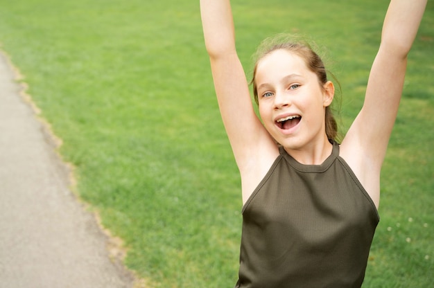 Happy teenage girl with hands up, contre green summer park. Espace de copie de portrait de jeune femme confiante