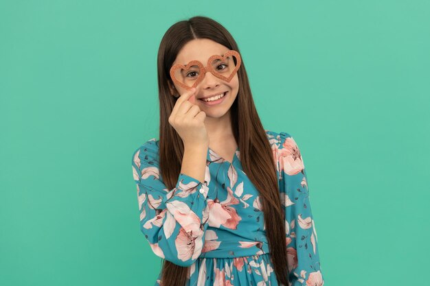 Happy tween girl smile portant des lunettes prop en forme de coeur pour la fête de la Saint-Valentin fond bleu le 14 février