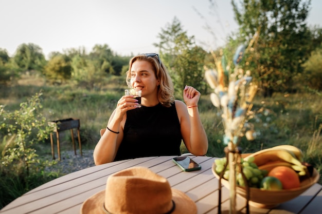 Happy Woman pigiste utilise le téléphone et boit un cocktail tout en se relaxant sur une tente de glamping confortable en journée ensoleillée Tente de camping de luxe pour les vacances d'été en plein air et les vacances Concept de style de vie