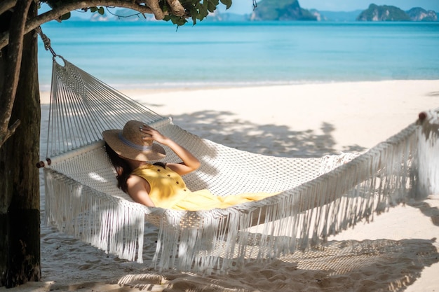 Happy Woman Traveler se détend dans un hamac sur la plage paradisiaque Une touriste en robe jaune se repose près de la mer tropicale vacances voyage été Wanderlust et concept de vacances