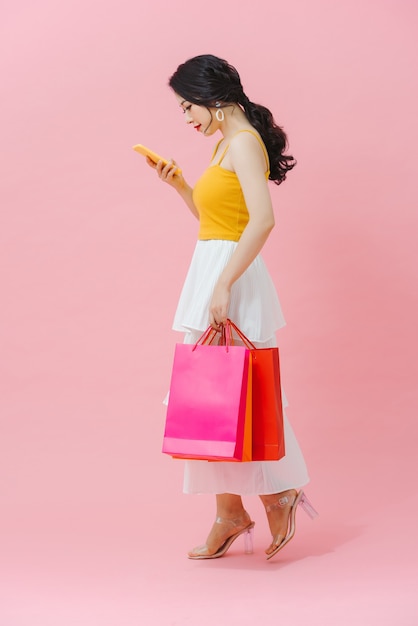 Happy young woman holding shopping bags et téléphone mobile sur fond rose