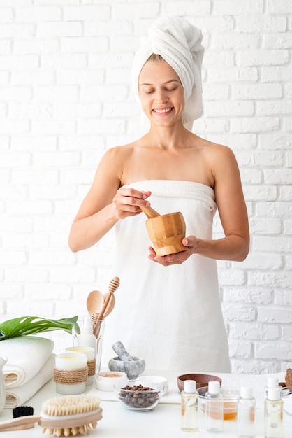 Happy young woman wearing white peignoirs serviettes sur la tête faisant des procédures de spa en mélangeant des ingrédients naturels dans un salon de beauté spa