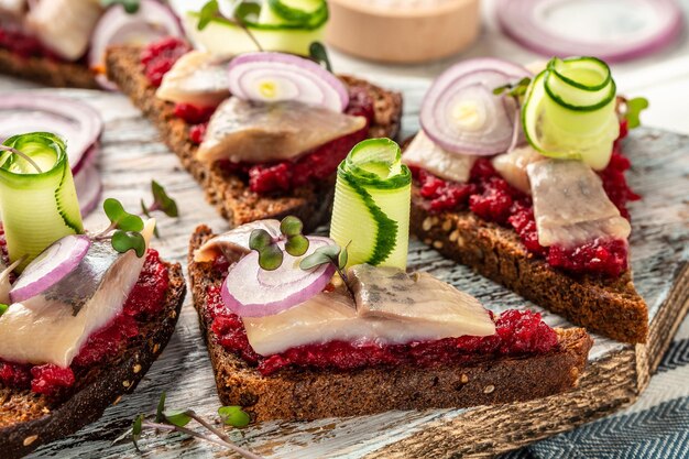 Hareng matie traditionnel avec salade de betterave concombre frais et rondelles d'oignon sur les toasts sur plaque blanche cuisine scandinave